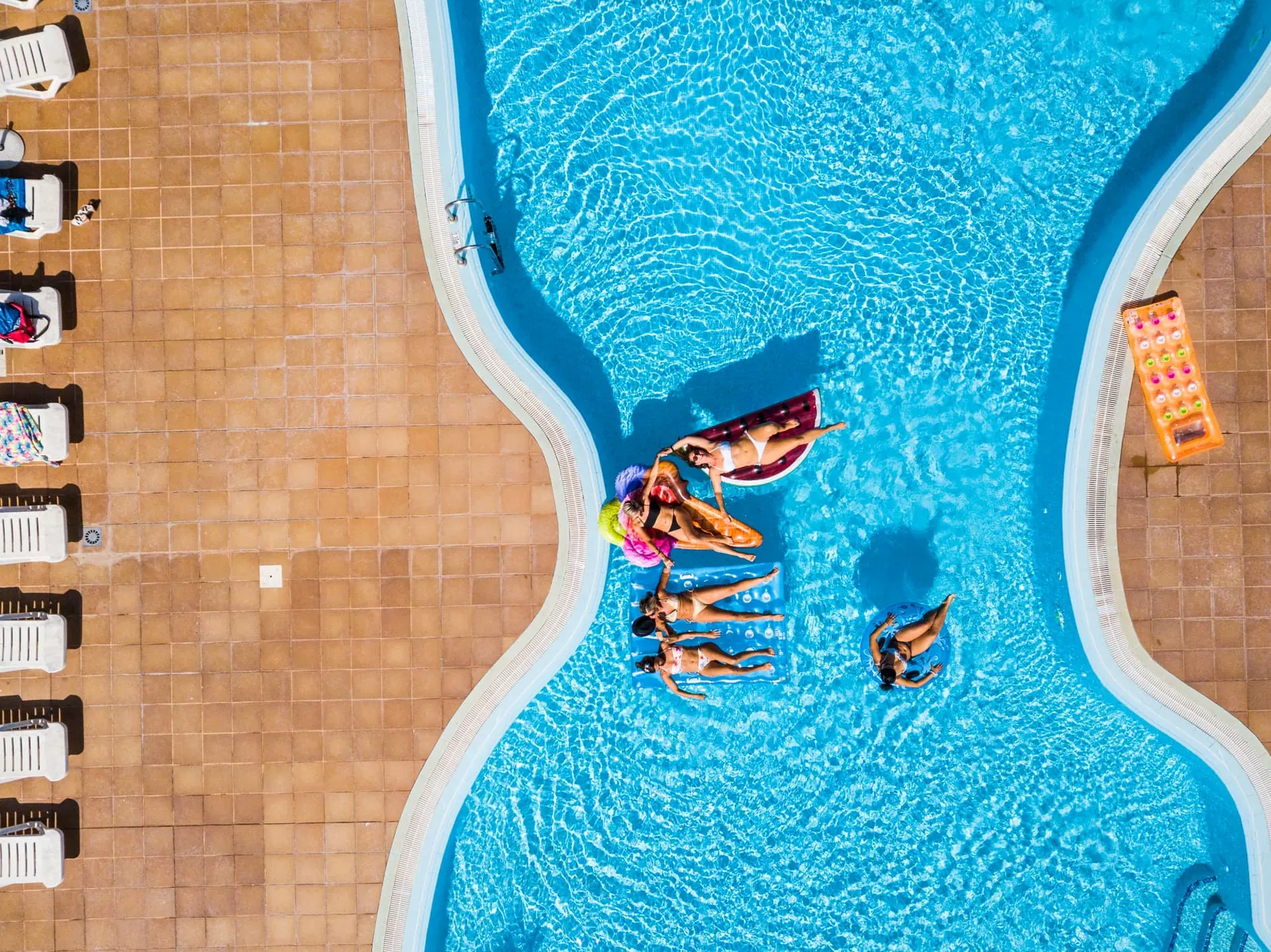 Aerial view of friends relaxing in a bright blue fiberglass pool with tiled deck in Las Cruces, NM Aerial view of friends relaxing in a bright blue fiberglass pool with tiled deck in Las Cruces, NM